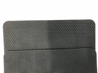 En närbild av en strukturerad, grå yta med två separata sektioner; toppen har ett bikakemönster, och undersidan har ett linjärt, räfflat mönster av Gummiduk SBR 70ShA Strukturerad.
