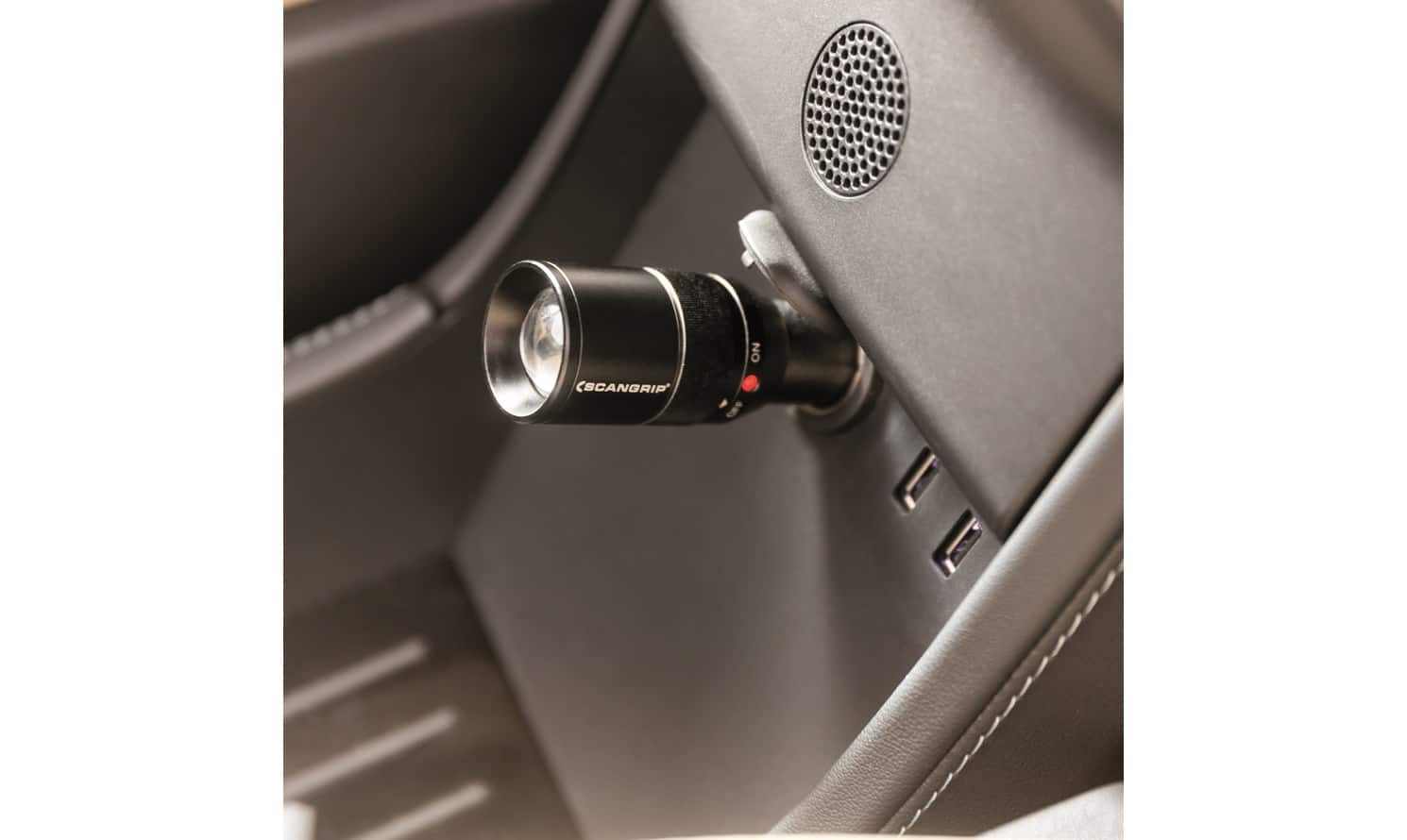 En svart pryl med etiketten "Ficklampa FlashPen 12V LED" ansluts till bilens invändiga uttag nära en högtalare och USB-portar.