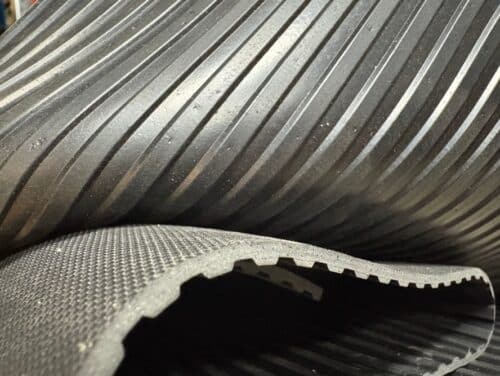 Närbild av två överlappande Gummimatta mellanräfflad-mattor: den övre mattan har ett räfflat mönster, medan den nedre har en ojämn, strukturerad yta.