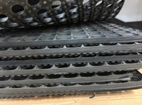 Närbild på staplade Gummimatta TrellComb S2225520 golvmattor av svart gummi, med texturerade ytor, runda hål och detaljerade kanter.